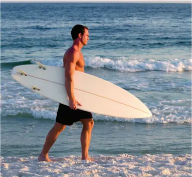  ??  ?? OPPOSITE: Enjoy a sunset cruise along the Emerald Coast. ABOVE: Surfer walking along Pensacola Beach..