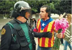  ??  ?? A man wearing a shirt with an Estelada (Catalan separatist flag) and holding carnations faces off with a Spanish Civil Guard officer outside a polling station for the banned independen­ce referendum in Sant Julia de Ramis, Spain, on Sunday.