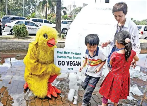  ?? JAY DIRECTO/AFP ?? A mother and her children look at a man wearing a chicken costume while holding a placard which reads ‘Meat melts the world. Harden your Resolve. Go Vegan’ while standing next to a melting igloo on a busy street sidewalk in Manila.