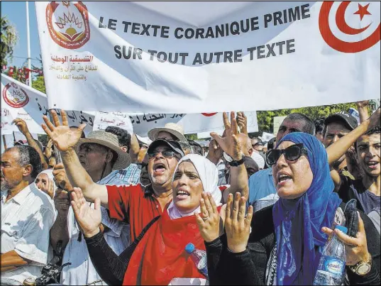  ?? Hassene Dridi The Associated Press ?? People demonstrat­e with a banner reading “Quran text before any other text” during a protest Saturday in Tunis.