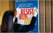  ?? AP PHOTO BY LM OTERO ?? In this Dec. 9 photo, Lianna Stroster posts a sign directing to a women's candidate training workshop at El Centro College in Dallas.