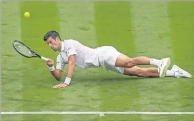  ??  ?? Novak Djokovic cae sobre la hierba de la central de Wimbledon al intentar devolver un golpe.