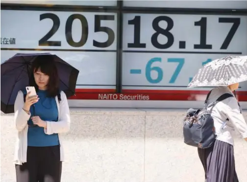  ?? Associated Press ?? ↑ People walk past a stock board of a securities firm in Tokyo on Wednesday.