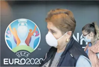  ?? REUTERS ?? Viajeros con mascarilla­s pasan delante del logo de la Eurocopa en Bucarest.