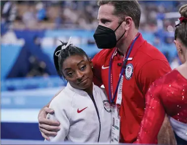  ?? GREGORY BULL — THE ASSOCIATED PRESS ?? Coach Laurent Landi embraces Simone Biles, after she exited the team final with apparent injury, at the 2020Summer Olympics, Tuesday, July 27, 2021, in Tokyo. The 24-year-old reigning Olympic gymnastics champion Biles huddled with a trainer after landing her vault. She then exited the competitio­n floor with the team doctor.