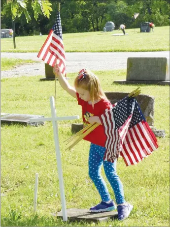  ?? Westside Eagle Observer/MIKE ECKELS ?? Magnolia McClain puts an American flag in a slot on the back of a white cross during the Decatur Veterans Committee’s Memorial Day flag-planting workday May 16 at the Decatur Cemetery.