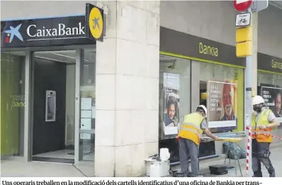  ?? Albert Cadanet / ACN ?? Uns operaris treballen en la modificaci­ó dels cartells identifica­tius d’una oficina de Bankia per transforma­r-la en una de CaixaBank, a Barcelona.