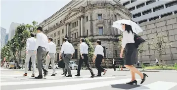  ??  ?? People walk past the Bank of Japan building in Tokyo, Japan. The Bank of Japan held steady on monetary policy yesterday as questions mount about when the central bank will start pulling the plug on its massive monetary easing campaign. — Reuters photo