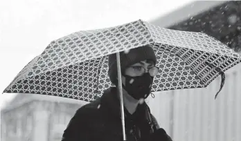  ??  ?? A woman wearing a mask because of the COVID-19 outbreak tries to stay dry as snow falls Thursday in Denver.