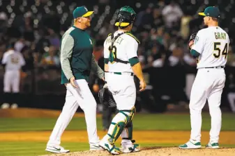  ?? Jason O. Watson / Getty Images ?? Pitching coach Scott Emerson (left) and catcher Josh Phegley approach the mound for a discussion with Sonny Gray.