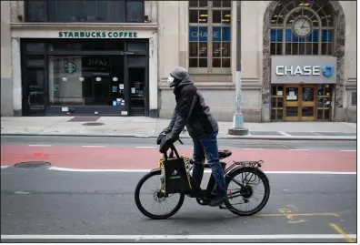  ?? (AP) ?? A Postmates delivery worker rides down a mostly empty Broadway in April in the Manhattan borough of New York. The pandemic has increased demand for third-party delivery orders while cutting into the ride-hailing businesses of companies such as Uber.