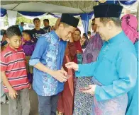  ??  ?? JAMAWI menyampaik­an duit raya kepada kanak-kanak yang hadir pada majlis itu.