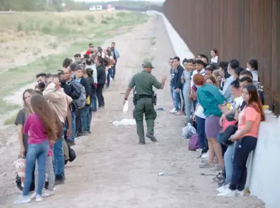  ?? DARIO LOPEZ-MILLS/AP FILES ?? A group of migrants stand next to the border wall in May as a Border Patrol agent takes a head count in Eagle Pass, Texas.