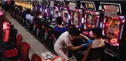  ?? Ap FiLe ?? NEXT! A woman receives the first shot of the Moderna COVID-19 vaccine as others wait for their turn in front of pachinko pinball machines at a pachinko parlor in Osaka, Japan, on Sept. 13.