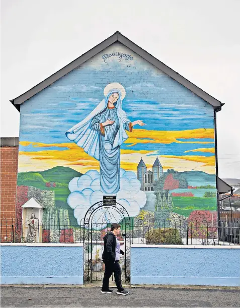  ?? ?? A woman walks past a Catholic mural yesterday as the latest census figures show that for the first time in Northern Ireland there are more Catholics than Protestant­s