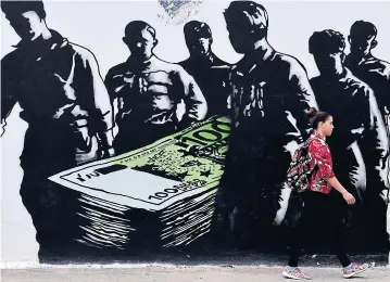  ?? AFP ?? A young woman walks past a graffiti called ‘Death of Euro’ by French street artist Goin, in central Athens yesterday.