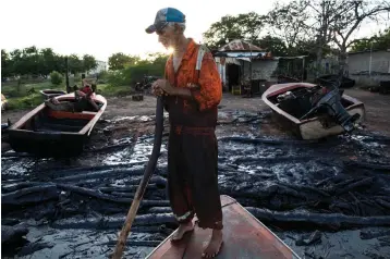  ?? Associated Press ?? ■ Fisherman William Vilchez stands on his boat May 18 on the oil-covered shoreline of Lake Maracaibo in Cabimas, Venezuela. The world’s largest crude reserves fueled an oil boom making Venezuela one of Latin America’s richest nations through the 1990s. But the boom has since turned to bust.