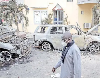  ?? — AFP photo ?? A man walking past the remains of two burned cars in Dakar, Senegal.