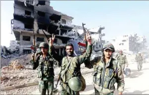  ?? LOUAI BESHARA/AFP ?? Syrian government forces gesture as they walk down a destroyed street on the southern outskirts of Damascus on Monday, after the Syrian army announced it was in complete control of the capital.