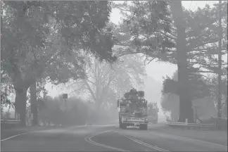  ??  ?? Utility trucks move down a smoke-filled State Road 12 on Monday in Kenwood, Calif., where wildfires have ravaged the area for days.