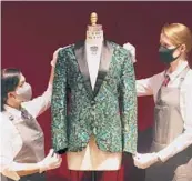  ?? JONATHAN BRADY/PA ?? Gallery assistants handle the oak leaf “glamouflag­e” jacket made for Mick Jagger, among other items on display at Christie’s, from the archive of fashion designer L’Wren Scott before it is offered at auction.