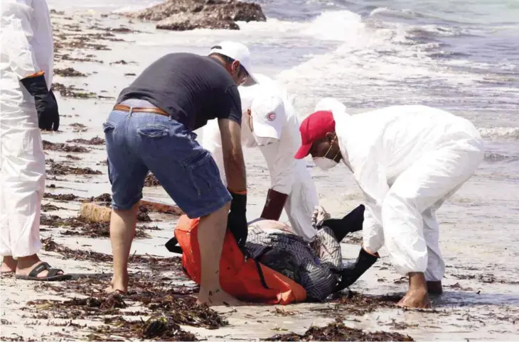  ??  ?? ZUWARA: Members of the Libyan Red Crescent, wearing protective white clothing and masks, collect the body of a migrant that had washed ashore on a beach yesterday in the port town of Zuwara, about 160 kms West of Tripoli, after two boats carrying...