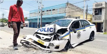  ?? FILE ?? A passer-by looks at a police patrol car that crashed into a wall along Slipe Road in Kingston on June 21. Columnist Patria-Kaye Aarons is no fan of throwing more money at the national security ministry to fight crime, especially if there are few...