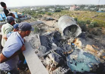  ?? Reuters ?? Palestinia­ns look at damage at the site of an Israeli air strike in Al Mughraqa on the outskirts of Gaza City yesterday.