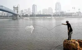  ?? JOSHUA A. BICKEL / AP ?? A man tosses a fishing net into the Ohio River as smoke from wildfires is visible over downtown Cincinnati on Wednesday.