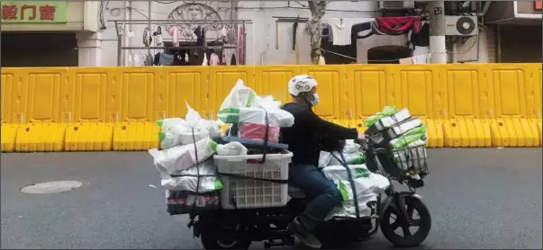  ?? (File Photo/AP/Chen Si) ?? A delivery man passes by barriers set up to lock down a community March 30 in Shanghai.