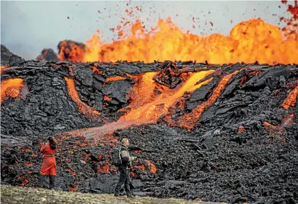  ?? AP ?? People look at the lava flowing on Fagradalsf­jall volcano, which is located 32 kilometres southwest of the capital of Reykjavik and close to the internatio­nal Keflavik Airport.