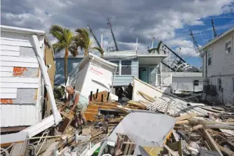  ?? AP PHOTO/REBECCA BLACKWELL ?? Kathy Hickey, 70, carefully picks her way through debris Oct. 5 from destroyed trailers in the mobile home park where she and her husband, Bruce, had a winter home on San Carlos Island in Fort Myers Beach, Fla., one week after the passage of Hurricane Ian.