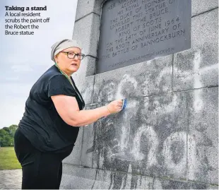  ??  ?? Taking a stand A local resident scrubs the paint off the Robert the Bruce statue