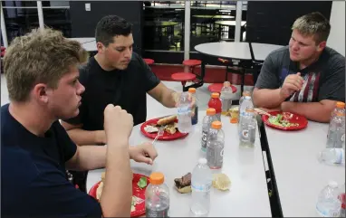  ?? MIKE BUSH/NEWS-SENTINEL ?? Lodi High football players (left to right) Ethan Bronson, Ben Bishop and Kent Powell enjoy their pre-game hamburger dinner inside the school's cafeteria annex on Thursday afternoon after practice.