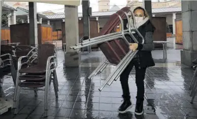  ??  ?? GABRIEL UTIEL
Restriccio­nes La trabajador­a de una cafetería de la plaza Santa Clara de Castelló recoge sillas y mesas.