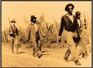  ?? Arkansas History Commission ?? In photo at left, Gov. Charles Hillman Brough (right) walks with an unidentifi­ed man as armed men look on in Elaine in early October 1919. In photo at right, black men are escorted by federal troops on a road near Elaine in early October 1919. More than 500 troops were taken to Elaine from Little Rock.