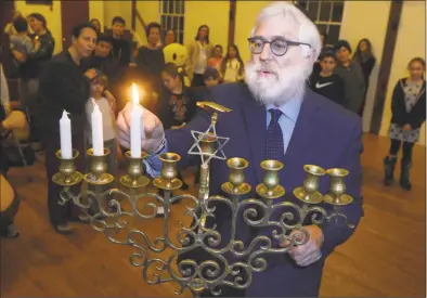  ?? Erik Trautmann / Hearst Connecticu­t Media ?? Rabbi Yehoshua Hecht, of Beth Israel Synagogue in Norwalk, lights the menorah during the Weston/Westport Hebrew School Family Fun Chanukah Event on Tuesday evening at the Norfield Grange in Weston. The Weston/Westport Hebrew School is accepting registrati­on for its new semester that begins Jan. 8. The after-school Hebrew schedule features the very popular Aleph Champ Hebrew reading and writing program for first- through seventh-graders, with a special curricula for kindergart­ners. The program also prepares students for bar and bat mitzvah.