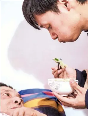  ?? DU HUAJU / XINHUA ?? Qi Jianguang feeds his father Qi Wenjiang at the farmhouse he rented near the constructi­on site where he works.