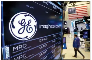  ?? AP/RICHARD DREW ?? The General Electric logo is displayed above a trading post on the floor of the New York Stock Exchange in June. GE said Monday that it is cutting its quarterly dividend by 50 percent as the company weighs the future of its transporta­tion, industrial,...