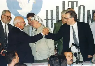  ?? ?? PALESTINIA­N AND Israeli top negotiator­s Abu Ala [left] and Uri Savir [right] shake hands after signing the second phase of the Oslo peace accords on September 24, 1995. PLO chairman Yasser Arafat is in the middle speaking to negotiator Saeb Erecat.