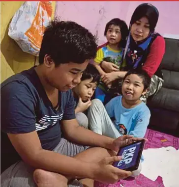  ?? BERNAMA PIC ?? Haslinah Hassan watching her eldest son, Muhammad Nur Izzat Ismail, use a tablet donated by preacher Ebit Lew, at their home in Kuala Lumpur yesterday.