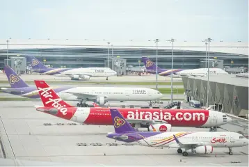  ?? WICHAN CHAROENKIA­TPAKUL ?? Aircraft belonging to carriers Thai Smile Airways, AirAsia and Thai Airways are seen parked on the tarmac at Suvarnabhu­mi airport yesterday.