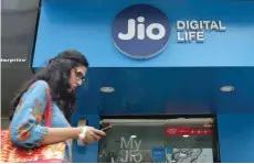  ?? — Reuters ?? A woman checks her mobile phone as she walks past a mobile store of Reliance Industries’ Jio telecoms unit in Mumbai.