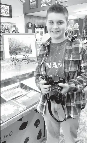  ?? SALLY CARROLL/MCDONALD COUNTY PRESS ?? Griffin Schutten captured the beauty of a cherry tree in bloom in the framed photo behind him at his booth at Rags To Riches Flea Market in Anderson. The young photograph­er and entreprene­ur utilized the beauty of the pink and white blooms as his...