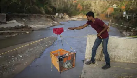  ?? DENNIS M. RIVERA PICHARDO/THE NEW YORK TIMES ?? Ramon Torres uses an improvised pulley system to transport supplies over a river where the bridge had been washed out, near Charco Abajo, Puerto Rico.