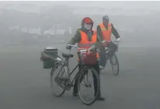  ?? STR/ AFP/GETTY IMAGES ?? Cyclists pass a toll booth on a smoggy highway in Jilin, China, last month. The U.S. and China are the two largest emitters of carbon dioxide.