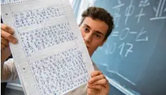  ??  ?? Abiturient Leon Habig hält eine Seite aus seinem Heft mit chinesisch­en Schriftzei­chen in der Hand. Auf der Tafel steht „Abitur 2017“in Chinesisch.
