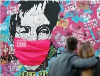  ?? Associated Press ?? ■ A couple look at the "Lennon Wall" with a face mask attached to the image of John Lennon, in Prague, Czech Republic. An annual tribute to John Lennon held in its adopted city of New York will go online. The five-hour event will be streamed for free on Lennon's birthday, October 9, starting at 6 p.m. on the LennonTrib­ute.org website.