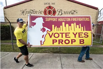  ?? Brett Coomer/Houston Chronicle via AP ?? ■ Houston firefighte­rs Jason Beasley, left, and Bucky Glenn carry a sign to a truck Sept. 25 as they prepare to talk to people about Propositio­n B, the pay “parity” item on the November ballot in Houston.