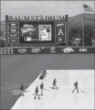  ?? NWA Democrat-Gazette/MICHAEL WOODS ?? The grounds crew pushes water off the infield tarp before the start of Friday’s scheduled game at Baum Stadium in Fayettevil­le. The game was postponed shortly thereafter and was reschedule­d as part of a doublehead­er today starting at 2 p.m.